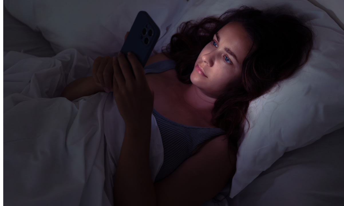 A woman laying in bed at night scrolling on her phone