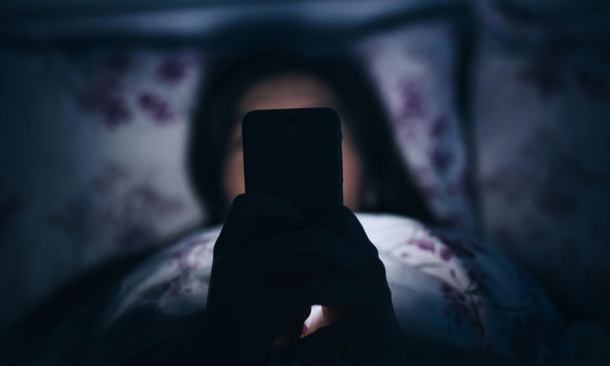 Woman reading and texting on smartphone in bed