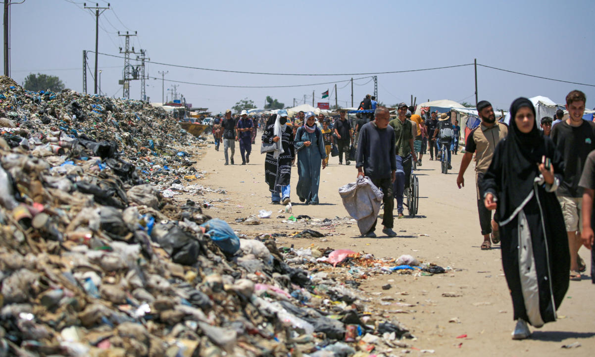People walk on a street littered with rubbish in Khan Yunis on the southern Gaza Strip on June 23, 2024,